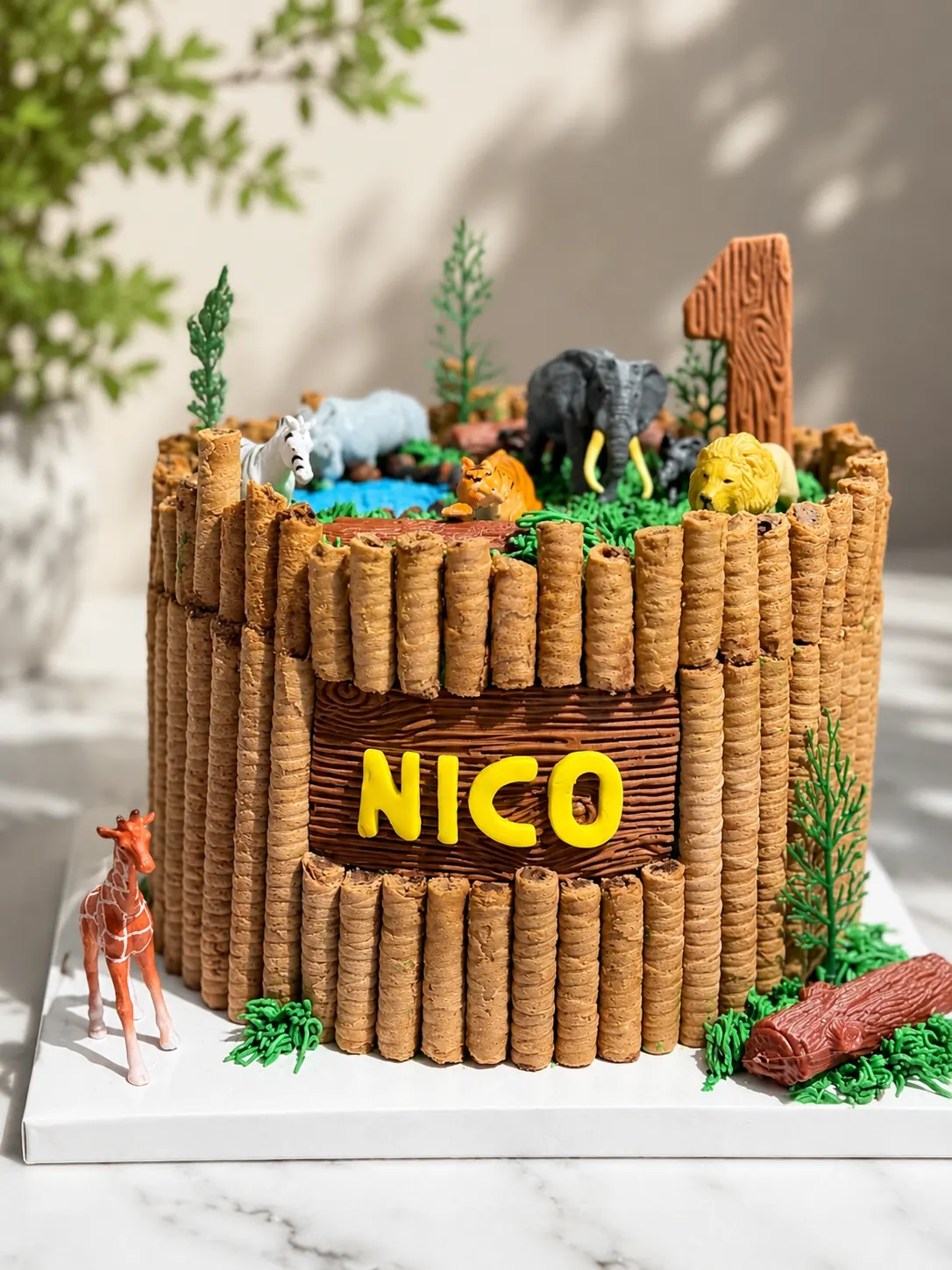 Torta temática de safari con figuras de animales, madera comestible y nombre frontal.