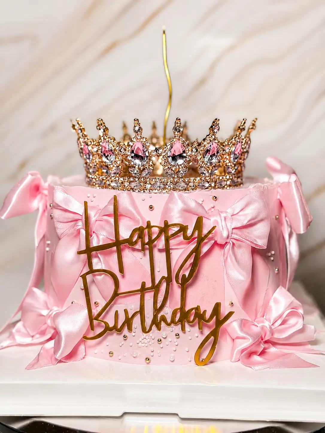 Detalle frontal de torta rosada con lazos y topper Happy Birthday.